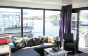 Lichte, moderne woonkamer op een woonboot met grote ramen en uitzicht op de jachthaven in Duitsland.