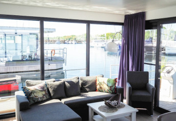 Lyst og moderne stue på en husbåd med store vinduer og udsigt over marina i Tyskland.