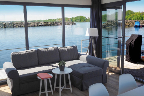 Stue med sofa og store vinduer, der giver udsigt over søen fra husbåd i Tyskland, Houseboat Family & Friends.