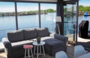 Woonruimte met grijze sofa en waterzicht op Houseboat Family & Friends met hond in Duitsland.