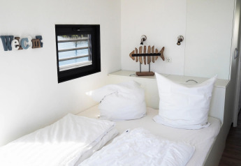 Bright, modern bedroom on a houseboat in Germany featuring a double bed, large pillows and fish art decor.