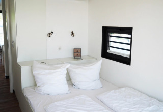 Dormitorio moderno en la casa flotante Family & Friends con perro, ropa de cama blanca y ventana pequeña.