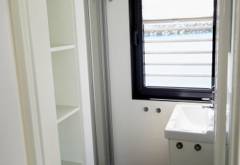 Salle de bain lumineuse sur une péniche avec grande fenêtre, lavabo et étagères, vue sur l'eau.