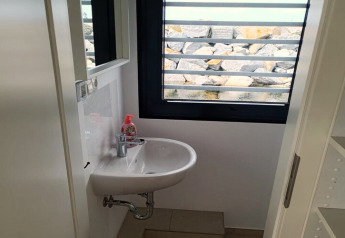 Kleine badkamer op een woonboot met wastafel, zeepdispenser en uitzicht op rotsen door het raam.