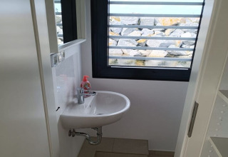 Petite salle de bain sur une péniche avec lavabo, savon et vue sur des rochers à travers la fenêtre.