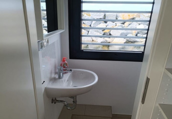 Small bathroom on a houseboat with a sink, soap dispenser, and a window view of rocks outside.