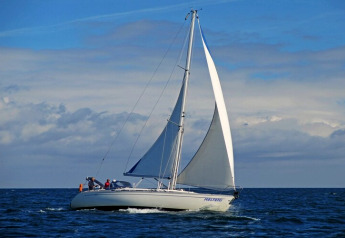 Zeilboot met twee personen op open water onder blauwe lucht, waarschijnlijk bij Duitsland, rustig varend.