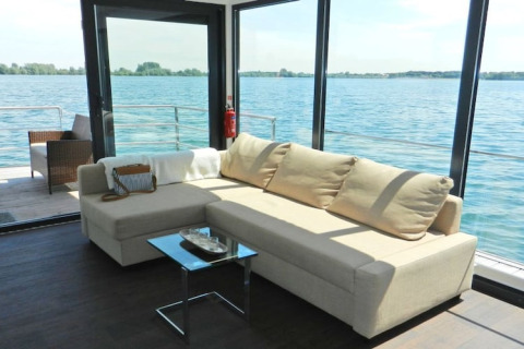 Luminoso soggiorno moderno su una houseboat con grandi finestre che si affacciano sull'acqua.