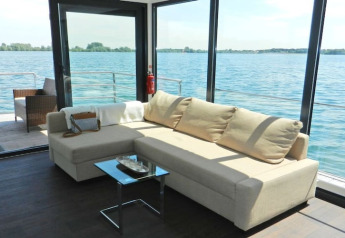 Bright and modern living area on a houseboat with large windows overlooking the water and deck.