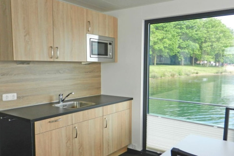 Cucina moderna in una casa galleggiante con grandi finestre vista lago e alberi verdi esterni.