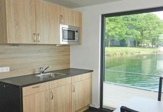 Moderne keuken op een woonboot met groot raam en uitzicht op het water en groene bomen buiten.