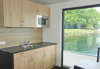 Cuisine moderne dans une péniche avec grande fenêtre offrant une vue sur un lac et des arbres verdoyants.