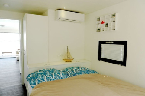 Slaapkamer op een woonboot voorzien van dubbel bed, airco, modelzeilboot en klein raam met rolgordijn.