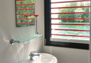 Houseboat bathroom featuring a window overlooking the water, glass shelf, mirror, and two orange flowers.