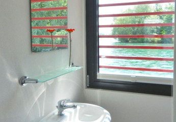 Houseboat bathroom featuring a window overlooking the water, glass shelf, mirror, and two orange flowers.