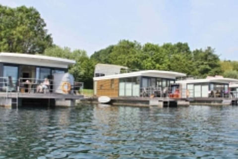 Moderne Hausboote liegen an einem ruhigen Gewässer, umgeben von üppigem grünen Wald und blauem Himmel.