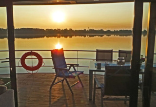 Zonsondergang op het dek van woonboot Floating 44 in Duitsland, met stoelen, tafel en reddingsboei.