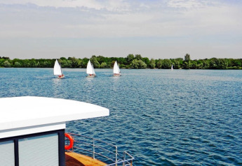 Vue depuis une péniche sur un lac avec plusieurs voiliers sur l'eau et des arbres verts en arrière-plan.