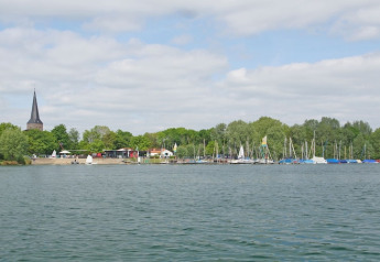 View from a houseboat of a lake with yachts, trees, and a church spire in the background.