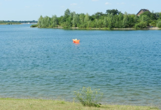 Et foto taget ved en husbåd med udsigt til en sø, en orange papirbåd og grønne træer i baggrunden.