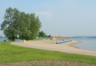 En fredelig udsigt over en tom strand med rækker af blå strandstole, grøn plæne og stille vand.