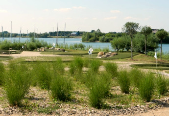 View of a mini-golf course by the lakeside with green vegetation, trees, and water in the background.