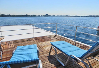 Sun deck of houseboat Floating 44 with two blue lounge chairs overlooking a lake in sunny Germany.
