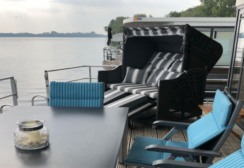 Espace détente extérieur sur une péniche en Allemagne avec fauteuils bleus et transat rayé, au bord du lac.