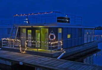 Maison flottante décorée de guirlandes lumineuses, amarrée le soir, photo prise en Allemagne.