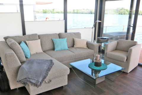 Moderne stue på en husbåd med udsigt over vandet, komfortabel sofa og glasbord i Tyskland.