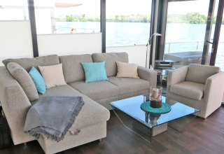 Moderne stue på en husbåd med udsigt over vandet, komfortabel sofa og glasbord i Tyskland.