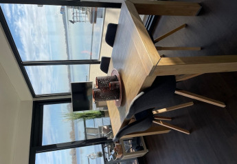 Dining table with black chairs on a houseboat, large windows overlooking the water, modern interior.