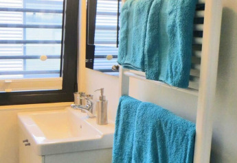 Modern houseboat bathroom with white sink, chrome soap dispenser, and blue towels on a heated towel rack.