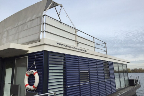 Flydende husbåd med moderne design og redningskrans ved www.hausboot-sonneninsel.de i Tyskland.