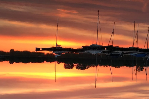 Solnedgang over vandet ved husbåd 'Floating 44 / Boot 2 / 3 Personen' i Tyskland, med refleksion af både.