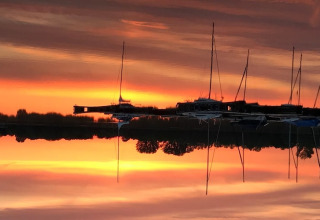 Solnedgang over vandet ved husbåd 'Floating 44 / Boot 2 / 3 Personen' i Tyskland, med refleksion af både.
