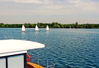 Uitzicht vanaf het woonboot Floating 44 met zeilboten op het meer, groene achtergrond in Duitsland.