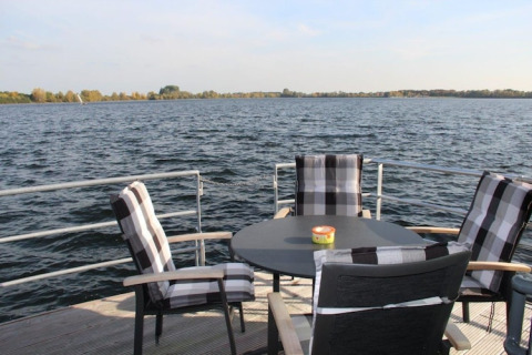 View from a houseboat deck with four plaid cushioned chairs around a round table overlooking the water.