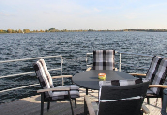 View from a houseboat deck with four plaid cushioned chairs around a round table overlooking the water.