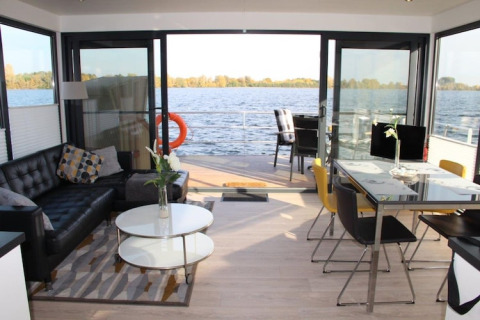 Modern houseboat interior with open glass doors, stylish living and dining areas overlooking calm water.