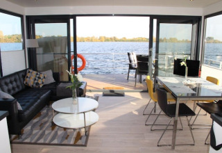 Interno di houseboat moderna con porte a vetri aperte, soggiorno elegante e vista sull’acqua tranquilla.