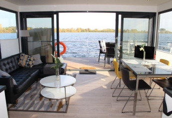 Modern houseboat interior with open glass doors, stylish living and dining areas overlooking calm water.