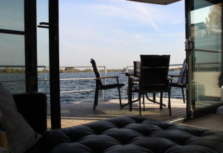 View from inside a houseboat looking through open doors at an outdoor table and chairs by the water.
