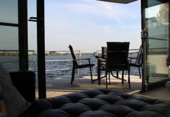 View from inside a houseboat looking through open doors at an outdoor table and chairs by the water.