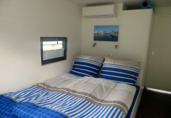 Slaapkamer op het woonboot Floating 44 / Boot 5 in Duitsland met blauw gestreept beddengoed en raam.