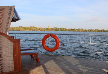 View from houseboat Floating 44 deck, showing lifebuoy, wooden floor, and scenic lake in Germany.