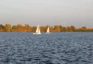 View from a houseboat overlooking a lake with two sailboats and autumn trees lining the shore.