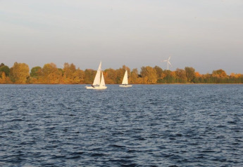 Vue depuis une péniche sur un lac avec deux voiliers et des arbres d'automne en arrière-plan.