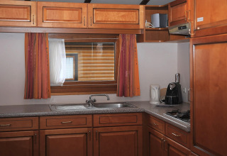 Knusse houten keuken met raam, oranje gordijnen en toestellen in Chalet Waldferienpark Gerolstein.