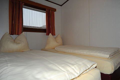 Slaapkamer met twee eenpersoonsbedden, zachte kussens en raam in chalet Waldferienpark Gerolstein 2, Duitsland.